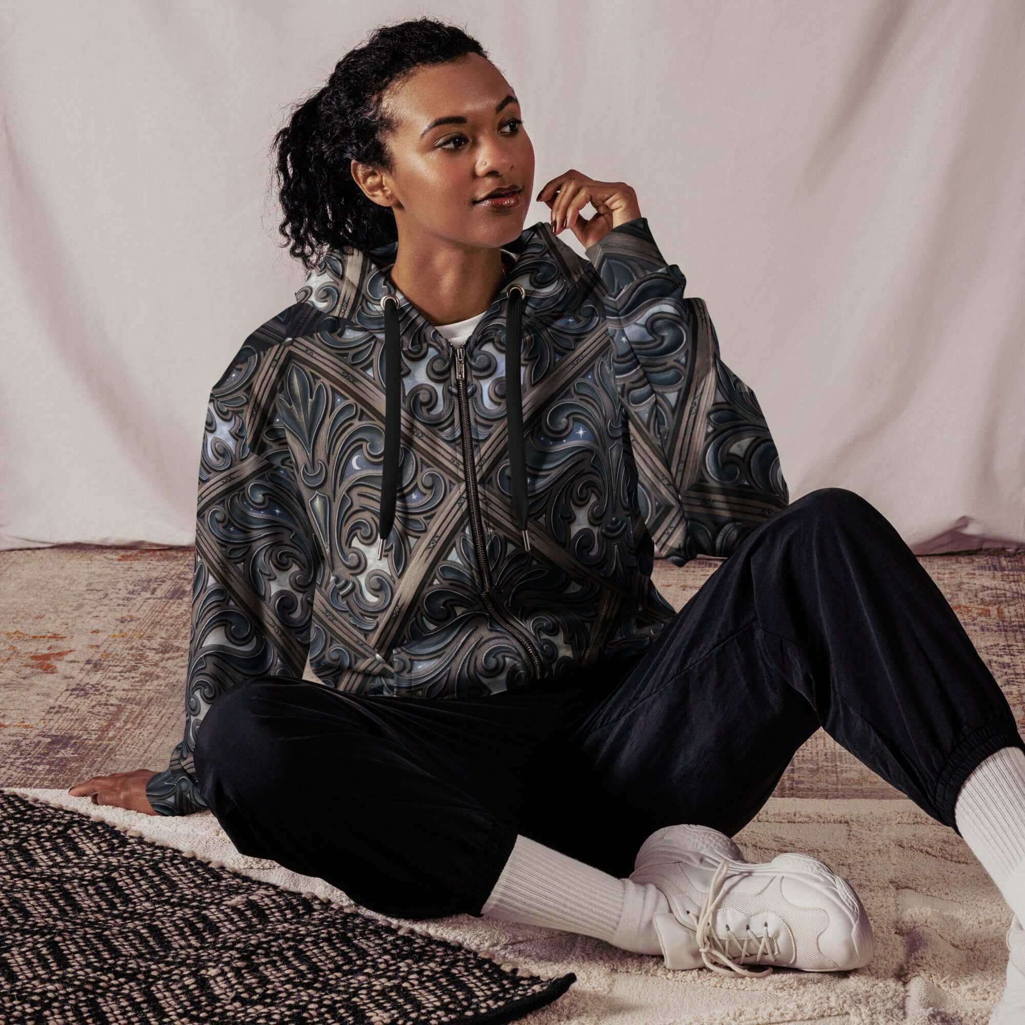 art deco filigree zip hoodie worn by a model sitting comfortably on a rug, showcasing the intricate pattern.