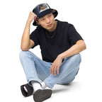 Young man wearing a reversible bucket hat streetwear, sitting casually in a black t-shirt and blue jeans.