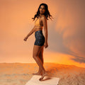 Model wearing Art Deco yoga shorts on a sandy beach background with an orange sunset.
